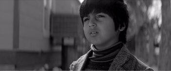 Movie still from “A Girl Walks Home Alone at Night” (2014), directed by Ana Lily Amirpour – A young boy wearing a sweater and a scarf; Close Up shot, Low angle