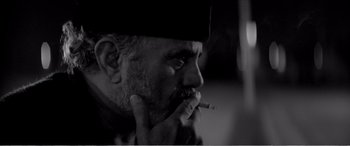 Movie still from “A Girl Walks Home Alone at Night” (2014), directed by Ana Lily Amirpour – A black and white photo of a man smoking a cigarette; Close Up shot, Low angle