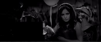 Movie still from “A Girl Walks Home Alone at Night” (2014), directed by Ana Lily Amirpour – A woman in a black dress is pointing at a table; Close Up shot, High angle