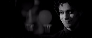 Movie still from “A Girl Walks Home Alone at Night” (2014), directed by Ana Lily Amirpour – A black - and - white photo of a man smiling at the camera; Close Up shot, Low angle