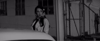 Movie still from “A Girl Walks Home Alone at Night” (2014), directed by Ana Lily Amirpour – A black and white photo of a woman standing next to a car; Medium shot, Low angle