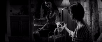 Movie still from “A Girl Walks Home Alone at Night” (2014), directed by Ana Lily Amirpour – A woman sitting in a chair holding a bowl of fruit; Medium shot, High angle