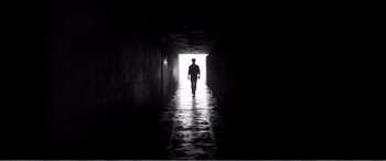 Movie still from “A Girl Walks Home Alone at Night” (2014), directed by Ana Lily Amirpour – A man walking down a dark hallway in the dark; Wide shot, Low angle