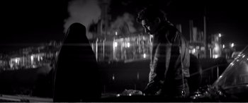 Movie still from “A Girl Walks Home Alone at Night” (2014), directed by Ana Lily Amirpour – A man standing in front of a window at night; Medium shot, Over the shoulder angle