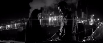 Movie still from “A Girl Walks Home Alone at Night” (2014), directed by Ana Lily Amirpour – A man and a woman standing next to each other in front of lights; Medium shot, Over the shoulder angle