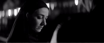 Movie still from “A Girl Walks Home Alone at Night” (2014), directed by Ana Lily Amirpour – A woman in a black headscarf is looking down; Close Up shot, Low angle