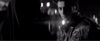 Movie still from “A Girl Walks Home Alone at Night” (2014), directed by Ana Lily Amirpour – A young man is standing in the dark with lights behind him; Close Up shot, Over the shoulder angle