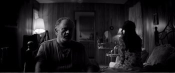 Movie still from “A Girl Walks Home Alone at Night” (2014), directed by Ana Lily Amirpour – An older man sitting in a living room next to a woman; Medium shot, Over the shoulder angle