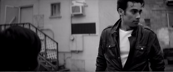 Movie still from “A Girl Walks Home Alone at Night” (2014), directed by Ana Lily Amirpour – A man wearing a leather jacket standing in front of a building; Medium shot, Low angle