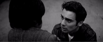 Movie still from “A Girl Walks Home Alone at Night” (2014), directed by Ana Lily Amirpour – A black - and - white photo of a man talking to another man; Close Up shot, Over the shoulder angle