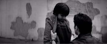 Movie still from “A Girl Walks Home Alone at Night” (2014), directed by Ana Lily Amirpour – A young boy holding his arm around another young person; Medium shot, Over the shoulder angle