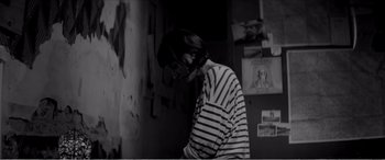 Movie still from “A Girl Walks Home Alone at Night” (2014), directed by Ana Lily Amirpour – A woman in striped shirt standing next to a wall; Medium shot, Over the shoulder angle
