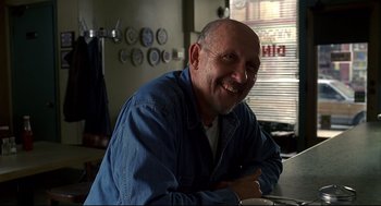 Movie still from “A History of Violence” (2005), directed by David Cronenberg – A man sitting at a table smiling for the camera; Close Up shot, Low angle