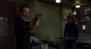 Movie still from “A History of Violence” (2005), directed by David Cronenberg – A man holding a gun in a room with people; Medium shot, Low angle
