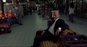 Movie still from “A History of Violence” (2005), directed by David Cronenberg – A man sitting on top of a wooden bench in a store; Wide shot, Low angle