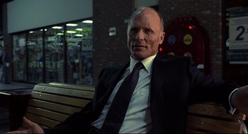 Movie still from “A History of Violence” (2005), directed by David Cronenberg – An older man wearing a suit and tie sitting on a bench; Medium shot, Low angle