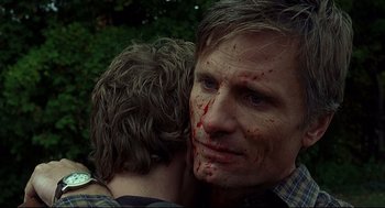 Movie still from “A History of Violence” (2005), directed by David Cronenberg – A man with blood all over his face is hugging another man; Close Up shot, Over the shoulder angle