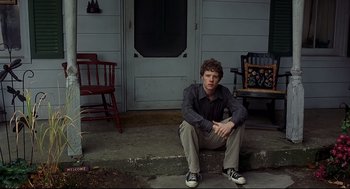 Movie still from “A History of Violence” (2005), directed by David Cronenberg – A man sitting on the steps of a house; Medium shot, Low angle