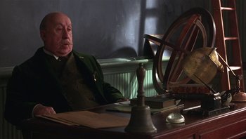 Movie still from “A Little Princess” (1995), directed by Alfonso Cuarón – An older man sitting at a desk in front of a clock; Medium shot, Low angle