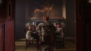 Movie still from “A Little Princess” (1995), directed by Alfonso Cuarón – A group of people sitting at a table in front of a painting; Wide shot, Over the shoulder angle