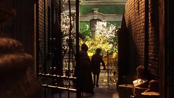 Movie still from “A Little Princess” (1995), directed by Alfonso Cuarón – Two people walking down a sidewalk near a brick building; Wide shot, High angle