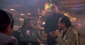 Movie still from “A Low Down Dirty Shame” (1994), directed by Keenen Ivory Wayans – A group of men sitting in a room talking to each other; Medium shot, Low angle