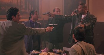 Movie still from “A Low Down Dirty Shame” (1994), directed by Keenen Ivory Wayans – A group of men standing around a table holding guns; Medium shot, High angle