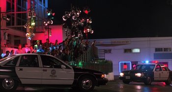 Movie still from “A Low Down Dirty Shame” (1994), directed by Keenen Ivory Wayans – A police car driving down a street next to a building; Extreme Wide shot, High angle
