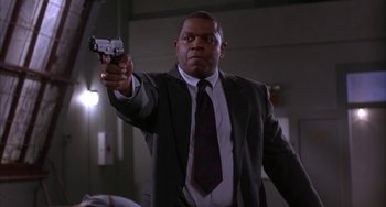 Movie still from “A Low Down Dirty Shame” (1994), directed by Keenen Ivory Wayans – A man in a suit and tie holding a gun in his hand; Medium shot, Low angle