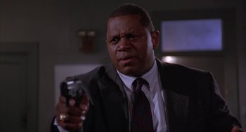 Movie still from “A Low Down Dirty Shame” (1994), directed by Keenen Ivory Wayans – A man in a suit and tie holding a gun; Close Up shot, Low angle