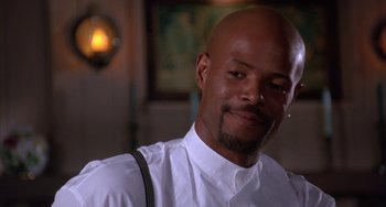 Movie still from “A Low Down Dirty Shame” (1994), directed by Keenen Ivory Wayans – A man with a beard is smiling for the camera; Close Up shot, Over the shoulder angle