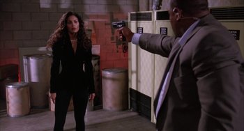 Movie still from “A Low Down Dirty Shame” (1994), directed by Keenen Ivory Wayans – A man in a suit and tie holding a gun pointed at a woman in a black suit; Medium shot, Over the shoulder angle