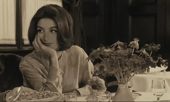 Movie still from “A Man and a Woman” (1966), directed by Claude Lelouch – A woman sitting at a table with a vase of flowers in front of her; Close Up shot, Over the shoulder angle