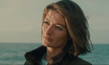 Movie still from “A Man and a Woman” (1966), directed by Claude Lelouch – A person wearing a jacket near a body of water; Close Up shot, Low angle