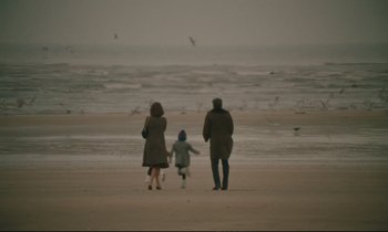 Movie still from “A Man and a Woman” (1966), directed by Claude Lelouch – Two adults and a child walking on the beach; Extreme Wide shot, High angle