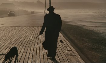 Movie still from “A Man and a Woman” (1966), directed by Claude Lelouch – A man walking on a boardwalk in the middle of the day; Wide shot, Low angle