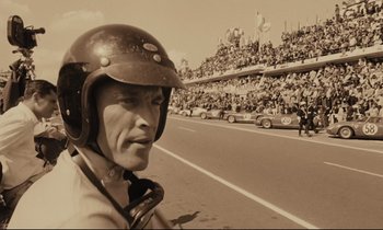 Movie still from “A Man and a Woman” (1966), directed by Claude Lelouch – A man wearing a helmet standing in front of a crowd; Close Up shot, Low angle