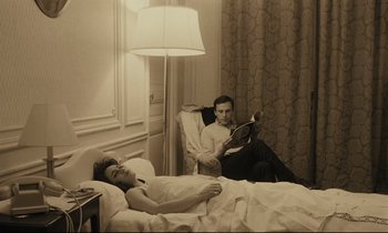 Movie still from “A Man and a Woman” (1966), directed by Claude Lelouch – A man reading a book in bed while a woman lies in bed; Medium shot, High angle