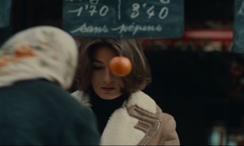Movie still from “A Man and a Woman” (1966), directed by Claude Lelouch – A woman is looking at an orange in front of a sign; Close Up shot, Over the shoulder angle
