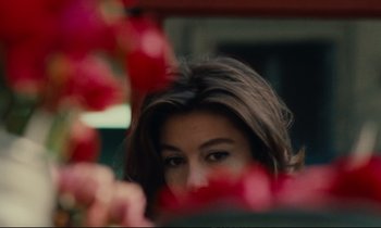 Movie still from “A Man and a Woman” (1966), directed by Claude Lelouch – A woman's face with red flowers in the background; Close Up shot, Over the shoulder angle