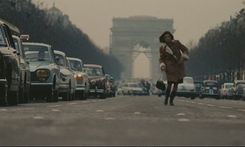 Movie still from “A Man and a Woman” (1966), directed by Claude Lelouch – A woman is running down the street with her purse; Wide shot, Low angle