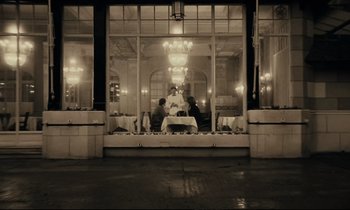 Movie still from “A Man and a Woman” (1966), directed by Claude Lelouch – A black and white photo of people sitting at a table in front of a window; Wide shot, Low angle