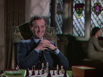 Movie still from “A Matter of Life and Death” (1946), directed by Emeric Pressburger – A man sitting at a chess board smiling for the camera; Medium shot, High angle