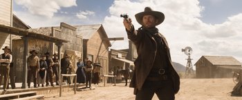Movie still from “A Million Ways to Die in the West” (2014), directed by Seth MacFarlane – A man holding a gun while standing on a dirt field; Medium shot, Over the shoulder angle