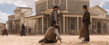 Movie still from “A Million Ways to Die in the West” (2014), directed by Seth MacFarlane – A man kneeling down next to another man in front of a building; Wide shot, Low angle