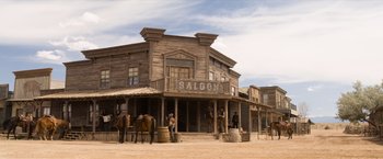 Movie still from “A Million Ways to Die in the West” (2014), directed by Seth MacFarlane – A man standing in front of a saloon with horses; Extreme Wide shot, Low angle