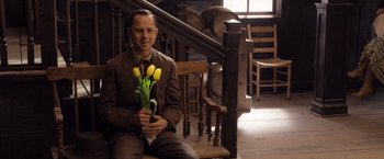 Movie still from “A Million Ways to Die in the West” (2014), directed by Seth MacFarlane – A man sitting on top of a wooden bench holding a bouquet of yellow flowers; Medium shot, High angle