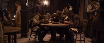 Movie still from “A Million Ways to Die in the West” (2014), directed by Seth MacFarlane – A group of men sitting around a table eating pizza; Wide shot, High angle