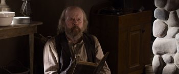 Movie still from “A Million Ways to Die in the West” (2014), directed by Seth MacFarlane – An old man sitting in a chair holding a book; Close Up shot, Low angle