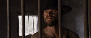 Movie still from “A Million Ways to Die in the West” (2014), directed by Seth MacFarlane – A man with a beard wearing a hat looking out of a jail cell; Close Up shot, Low angle
